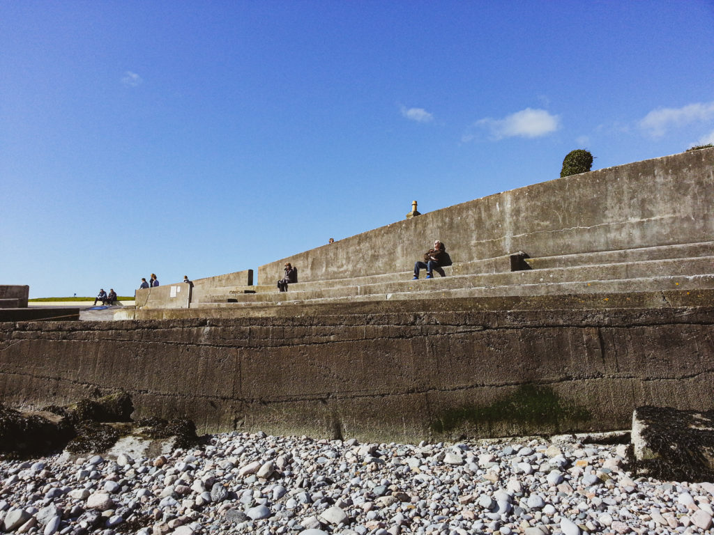 Locals enjoy the morning sun sitting on the concrete steps at Black Rock Beach